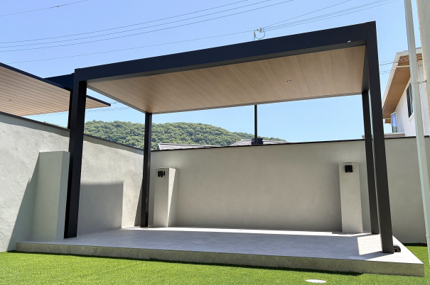 赤穂市新築外構庭にあるテラス タカショーのホームヤードルーフⅡシングル仕様屋根直線色はマットブラックポリカはクリアマット 内天井屋根シングル仕様色はくり柾目。タイルデッキはオオムラエコストーン色はグレーの様子